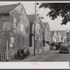 Commercial Street, the main street of Provincetown which runs along the waterfront, including a view of the "Sand Bar Club" and the tourist bus which runs out to the beach. Provincetown, Massachusetts.