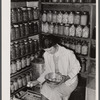 Mrs. Richard R. Gill, Donley County, Texas, prepares eggs for the market. The large containers are filled with homemade lard for this work grant family. Note that Mrs. Gill's attractive jacket is made from a sugar sack.