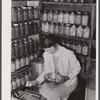 Mrs. Richard R. Gill, Donley County, Texas, prepares eggs for the market. The large containers are filled with homemade lard for this work grant family. Note that Mrs. Gill's attractive jacket is made from a sugar sack.
