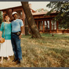 Two people stand outside in front of house