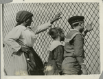 A woman, a boy and a girl at a chain link fence, Ellis Island, New York