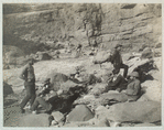 A Noonday Rest in Marble Canyon, showing well the head of a fall. Snapshot by James Hogue, 1890. From left to right, Travers (standing), Hislop, Kane, Gibson, Ballard, Edwards, Twining (standing), Stanton, McDonald, Brown.