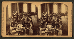 View of women seated at a long table sewing.