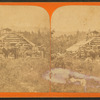 Men with fishing poles, rifles and pistols posed outside a log cabin at Kennebago Lake.