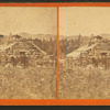 Men with fishing poles, rifles and pistols posed outside a log cabin at Kennebago Lake.