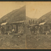 Group in front of a log cabin with a covered wagon.