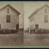 View of a two-story wood-frame school house with students and teachers out front.