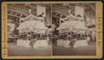 Interior of a large hall showing booths set up for a fair.