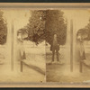Man and woman, with parasol, standing behind double fountain.