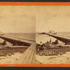 Pier extending from a sandy shoreline.