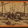African-American longshore men and bales of cotton on the dock.