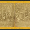 Group portrait of people in front of cottage, including furniture in a moving wagon.