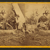 Studio view of hunters at dinner, showing camp, dead deer and hunting dog.