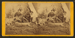 Studio view of hunters at dinner, showing camp, dead deer and hunting dog.