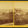 Field scenery in foreground with houses in background.