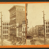 Street scene with buildings, street tracks, wagons.