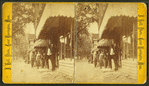 View of a group of men in front of a store, one holding a hose.