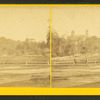 Two people standing next to a fence with trees and a large institutional structure in the background.