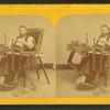 Studio portrtait of a man, possibly handicapped, in specially outfitted chair where he is shown building picture frames.