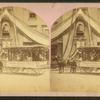 Decorated wagon with women riding in it, banner on side reads "followers of Betsy Baker preparing and braiding domestic straw," in front of building with bunting.