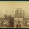 View of a fire in large industrial building with men spraying water.