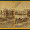 View of a waterfall with buildings lining the river on the opposite shore.