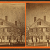 Group playing croquet under budding trees in front of large wood frame house.