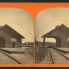 View of railroad depot with shed roof over tracks.