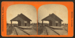 View of railroad depot with shed roof over tracks.