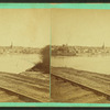 View of railroad tracks with river and city beyond.