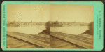 View of railroad tracks with river and city beyond.