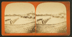 Water pouring over a dam, men in boat peering over spillway.