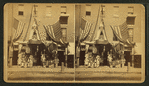 View of a store front decorated with flags with goods displayed.
