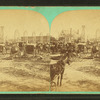 Buggies and wagons gathered around building under construction.