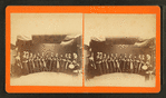 Studio view of a group of women holding brooms(?) and 1 woman with a drum.