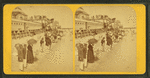 People on the beach in front of the Plank Walk, some with umbrellas.