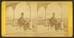 View of a man with a beard and top hat on a porch.