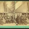 Group of men formally posed in front of large tent with sign that reads "Warren".