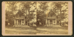 View of a cottage, trees in front, people on porch.