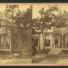 View of a cottage, trees in front, people on porch and balcony.