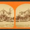 People sitting in the yard, on the porch, and balcony of a cottage.