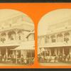 People gathered in front of and on the balcony of a large building, hanging sign reads, "Wesley House ice cream".