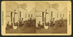 View of men and a child in a yard with a wood carving of a woman holding a pole topped with a weathervane.