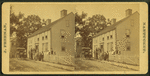Group posing on porch of large house, possibly a boarding house, with wagonette standing by.