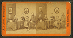 Studio portrait of family, stereo-viewer on table, one girl with book.