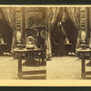 Interior showing oriental vase, drapes in the door, an object in a bell jar, ornate picture frames.
