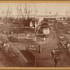 Barrels and cargo on piers, ships in background.