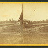 General view with, road, buildings, and smokestacks in the distance.