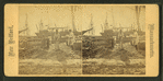 Men working on wharf in front of moored sailing vessels.