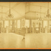 Interior of large room with piano, statues, benches and chairs lining it.